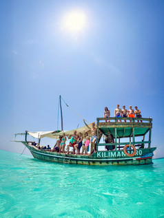 skupina ljudi na leseni ladji z napisom Kilimanjaro sredi turkiznega morja