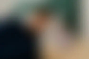 A lavender candle with soft purple wax glowing on a cream nightstand, beside a young man peacefully sleeping under a navy blanket with golden stars.