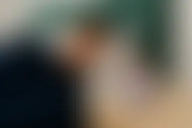 A lavender candle with soft purple wax glowing on a cream nightstand, beside a young man peacefully sleeping under a navy blanket with golden stars.