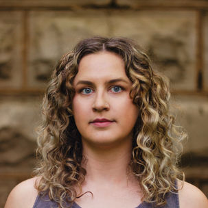 headshot of a young white woman with curly dirty blonde hair wearing a dark grey tank top
