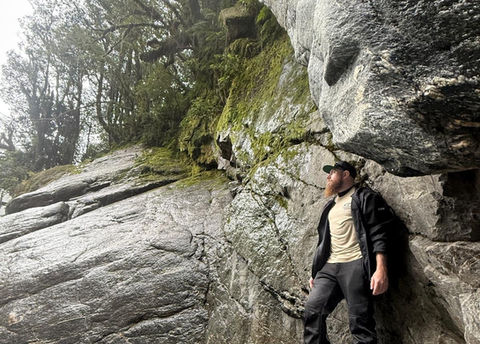Dakota standing on rocky riverbed near moss-covered cliffs in hiking gear