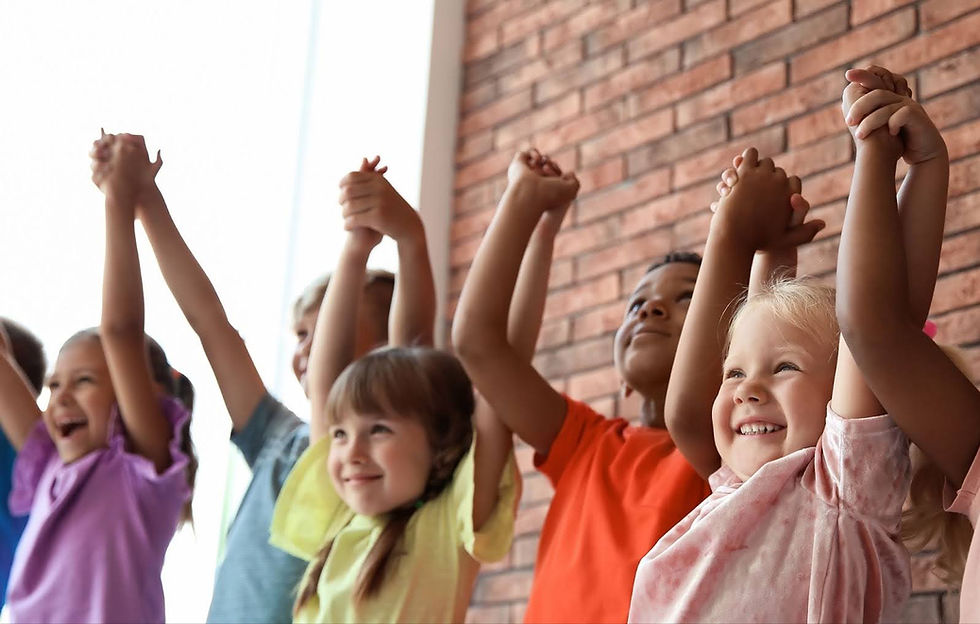 Children holding hands up, cheering in front of a brick wall. Their colorful clothes and big smiles convey joy and excitement.