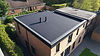 Bild: Flachdachhaus mit schwarzer Dachabdichtung, roten Ziegelwänden und umliegendem Grün