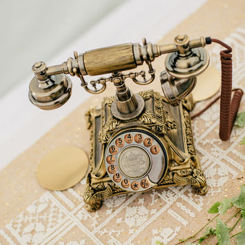 Antikes, ornamentiertes Wähltelefon auf einem Tischläufer.