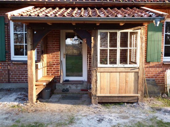 Holzüberdachung mit Sitzbank und Fenster vor rotem Backsteinhaus