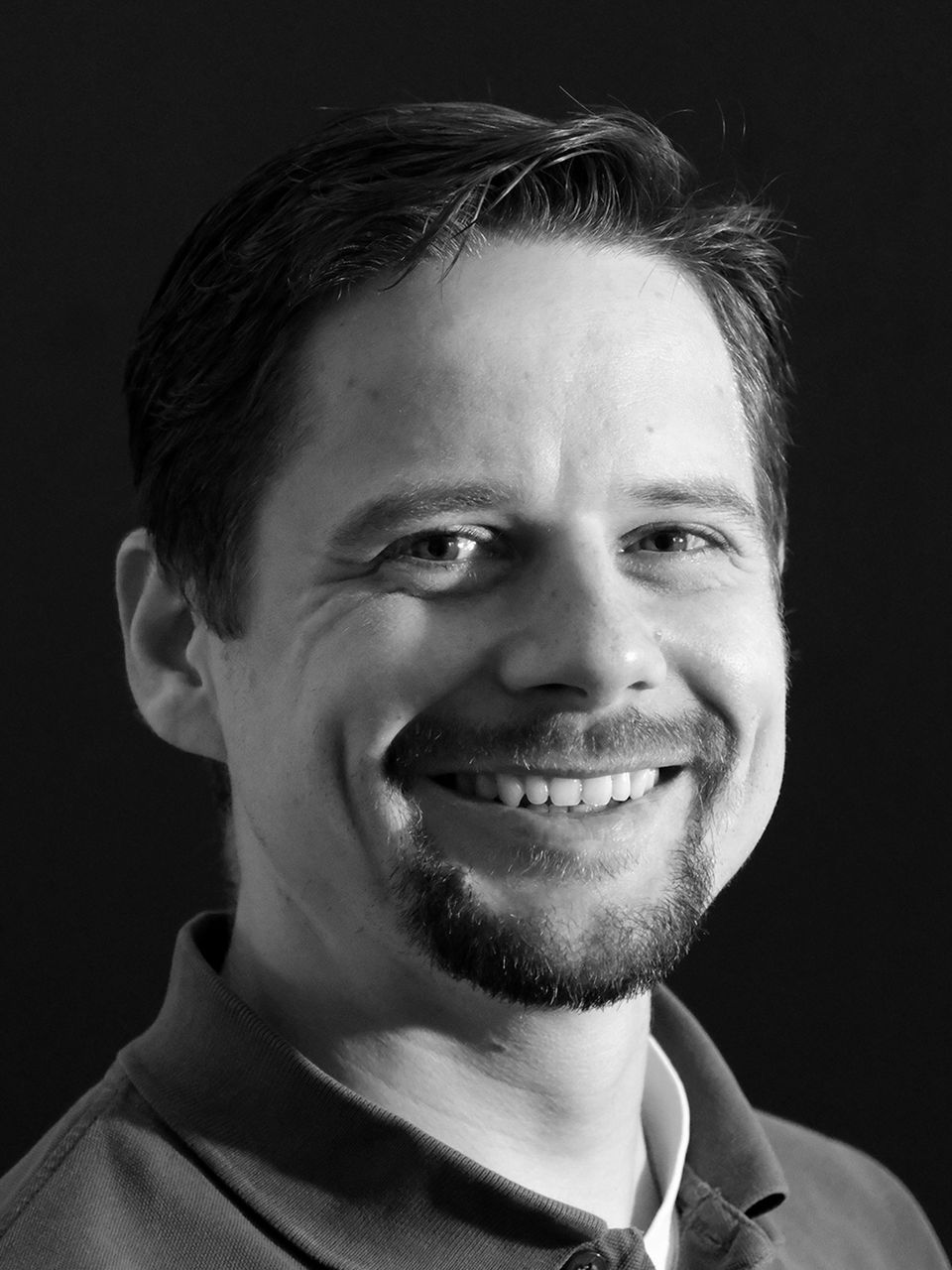 Lächelnder Mann mit Bart im Schwarz-Weiß-Porträt.