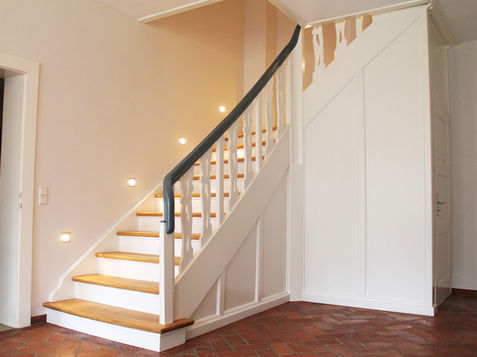 Elegante weiße Podesttreppe mit braunen beleuchteten Holzstufen und einem schwarzen Geländer