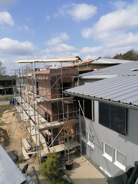 Baustellenbild mit einem Anbau aus Ziegelmauerwerk, umgeben von einem Baugerüst