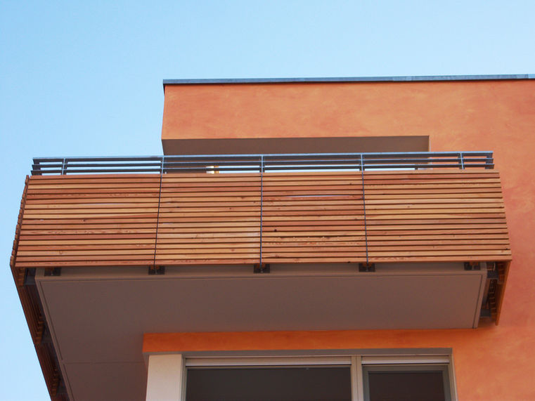 Bild: Modernes Flachdachhaus mit holzverkleidetem Balkon und orangefarbener Putzfassade