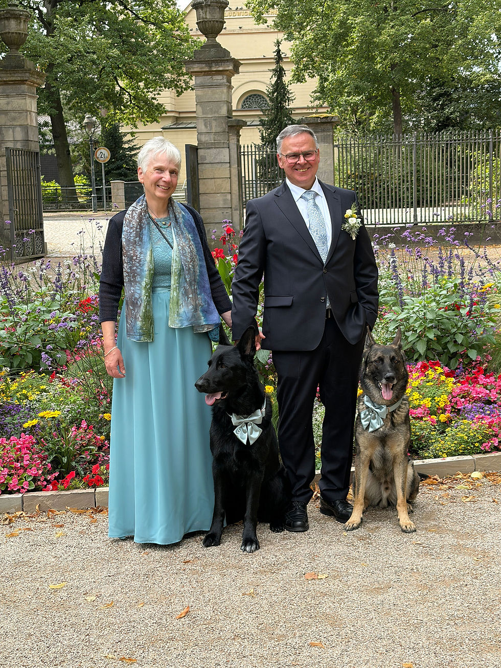 Hochzeitspaar mit zwei Hunden vor historischem Gebäude in einem farbenfrohen Blumengarten