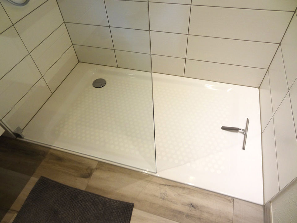 Saubere, helle Duschkabine mit Duschwanne und Abzieher, moderne, helle Fliesen