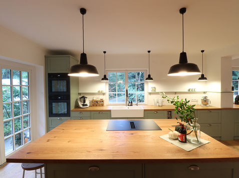 Geräumige und offene salbeigrüne Landhausküche mit Kochinsel und Holztheke mit Ausgang zur Terrasse