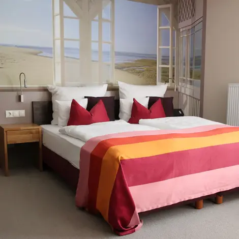 Ankerlink Doppelzimmer: Foto eines Doppelbettes mit Nachttisch vor einem Küsten-Hintergrund