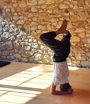 Person doing a headstand pose with stone wall background yoga retreats in greece.