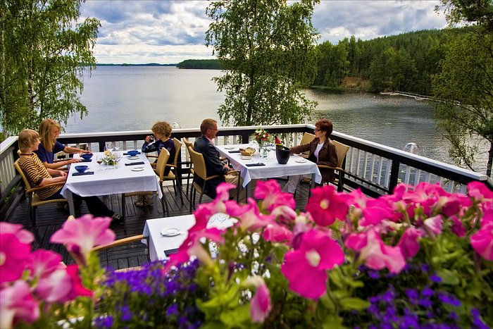 Flowers on a deck with tables and chairs, people enjoying dinner with a lake view