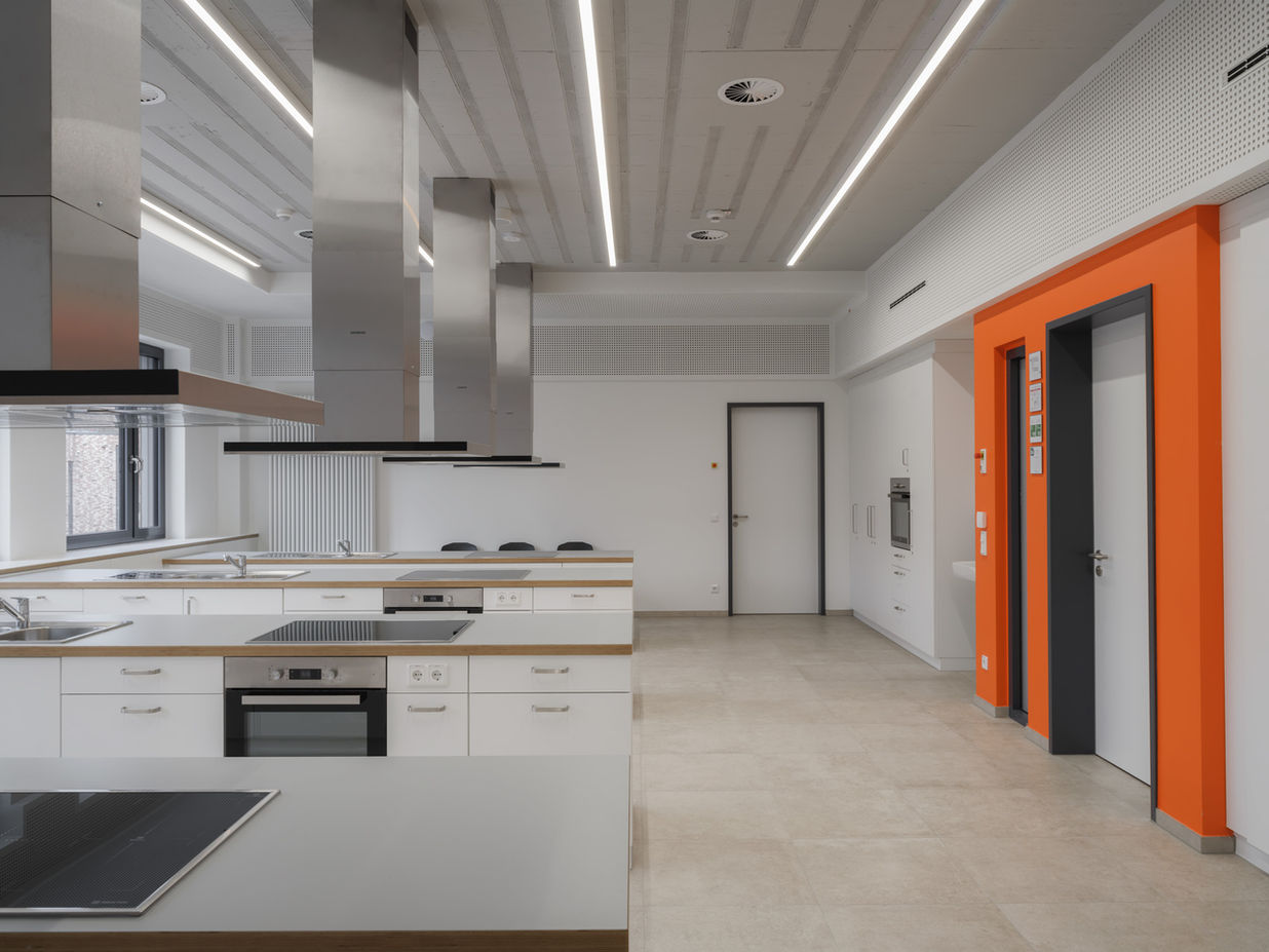 Teaching kitchen in Bildungscampus Unna — central kitchen islands with orange architectural accents