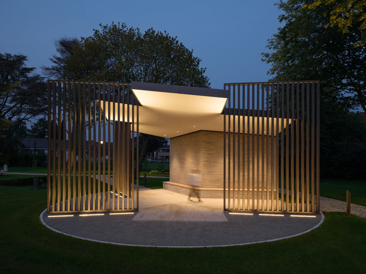 Cemetery pavilion Werlte at blue hour — illuminated steel structure forming a cross-like spatial composition