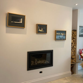 Modern living room with built-in fireplace, firewood stack, framed pictures, chair with throw blanket, and tiled floor.
