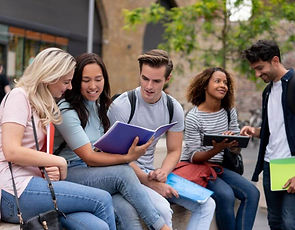 Five young men and women of different races sat outside, happily chatting and sharing notes. They looked like they were discussing academic or work-related topics.