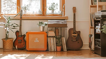 一個家庭音樂角落，展示了兩把吉他、一個橙色的揚聲器、一台轉盤唱機和一排唱片。房間內有綠色植物，窗外透進陽光，營造出溫馨而有創意的氛圍。