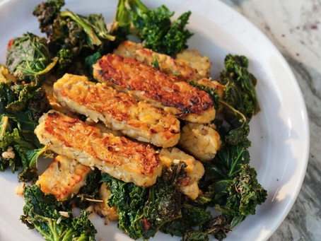 Golden tempeh strips with sauteed kale in a white bowl