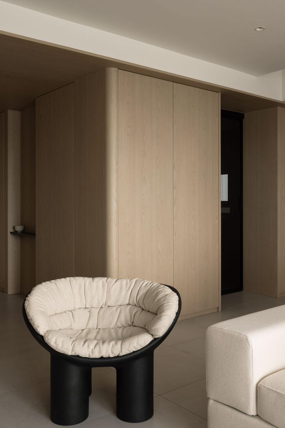 Introspective Apartment – View from the light timber-clad foyer towards the living room, framed by full-height panels and a softly illuminated threshold.