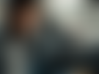 Um motorista com expressão de estresse e cansaço mental, sentado dentro de um carro, com a mão na cabeça, olhando para o lado. O celular com aplicativo de navegação está preso ao painel e um copo de café vazio está no console. O fundo mostra uma cidade com trânsito leve e prédios.