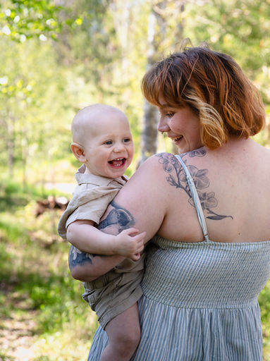 Mamma med skrattande bebis under familjefotografering utomhus