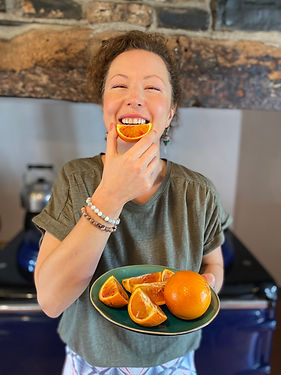 Woman happy and smiling eating oranges whilst holding a plate of orange slices