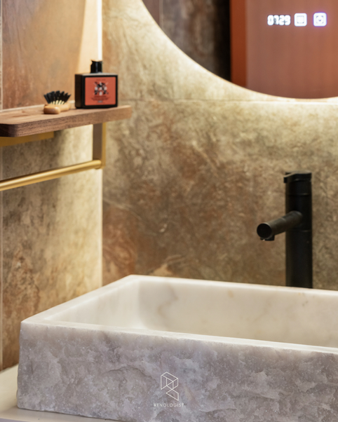 Stone basin with a matte black tap, warm backlit mirror and wood shelf in a luxury HDB bathroom.