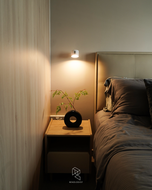 Modern bedroom with a wood bedside table, upholstered bed, warm wall lighting, and minimalist contemporary design.