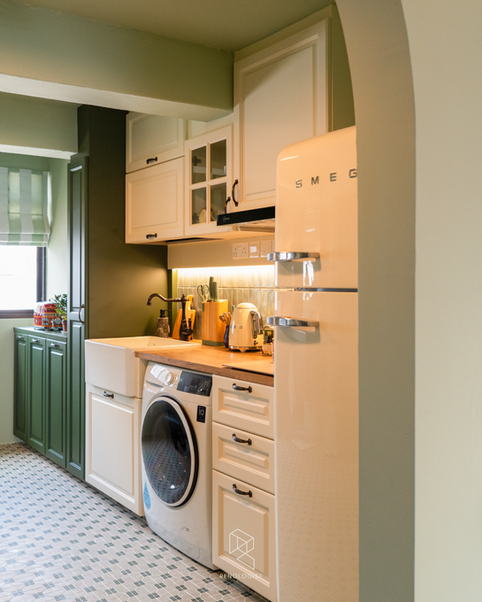 English Cottage Farmhouse kitchen with classic white shaker cabinetry, deep green base cabinets, sage green tile backsplash, warm wood countertop, farmhouse apron sink, vintage bridge faucet, and patterned mosaic floor tiles.