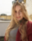"Porträt einer jungen blonden Frau mit strahlendem Lächeln und natürlicher Schönheit. Sie hat lange blonde Haare und trägt ein elegantes Outfit. Der Hintergrund ist verschwommen, um den Fokus auf ihr Gesicht und ihre Ausstrahlung zu legen.
