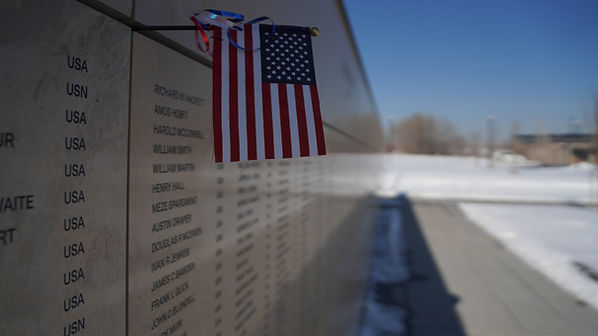 memorial wall with list of engraved names, American Flag in foreground