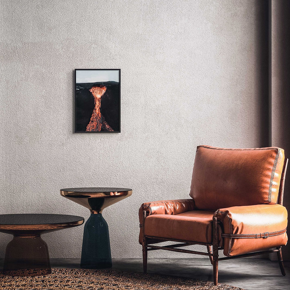 Thumbnail: Black framed print of an active volcano crater, with flowing lava, hung above an armchair