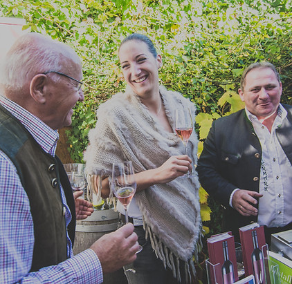 Gäste genießen Weinverkostung im malerischen Weingarten des Weinhaus Grafing, umgeben von grünen Reben.