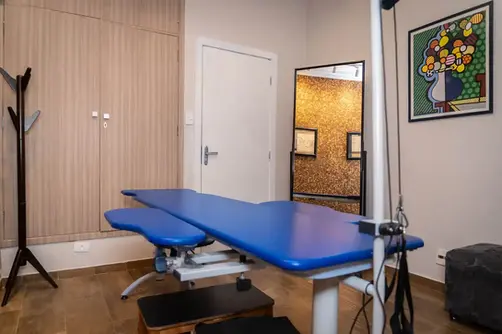 Sala de terapia com maca de RPG e mesa de escritório