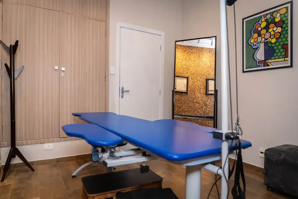 Sala de terapia com maca de RPG e mesa de escritório
