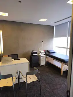 Consultório com maca e equipamentos elétricos/eletrônicos para tratamento físico-muscular.
