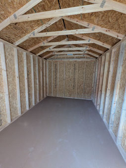 Interior view of a 10x16 utility shed with extra-height walls, exposed wood framing, OSB walls and ceiling, and unfinished floor space for tools and equipment storage.