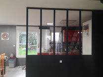 Intérieur avec verrière d'atelier, séparation noire et cuisine. Métal brut et éléments décoratifs.