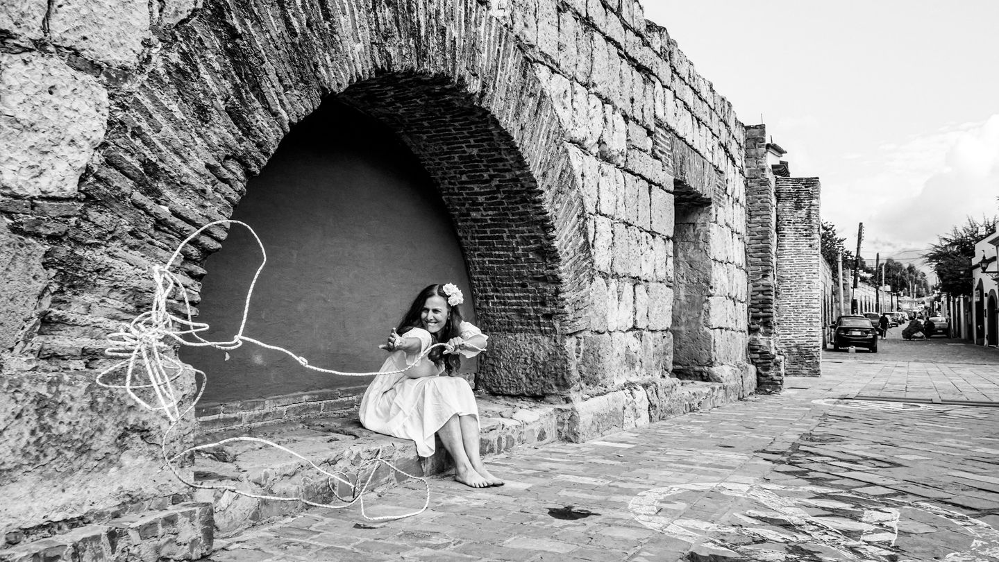 Reflective black-and-white photo performance from “A Transformation Machine,” blending urban and cultural landscapes with expressive movement, capturing themes of womanhood, personal growth, and liberation through self-discovery.