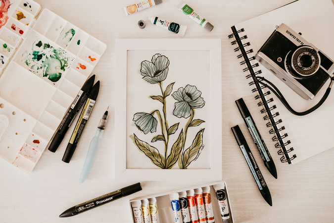 Artwork showing a blue wildflower painting, paints, markers, notebooks, and a camera.