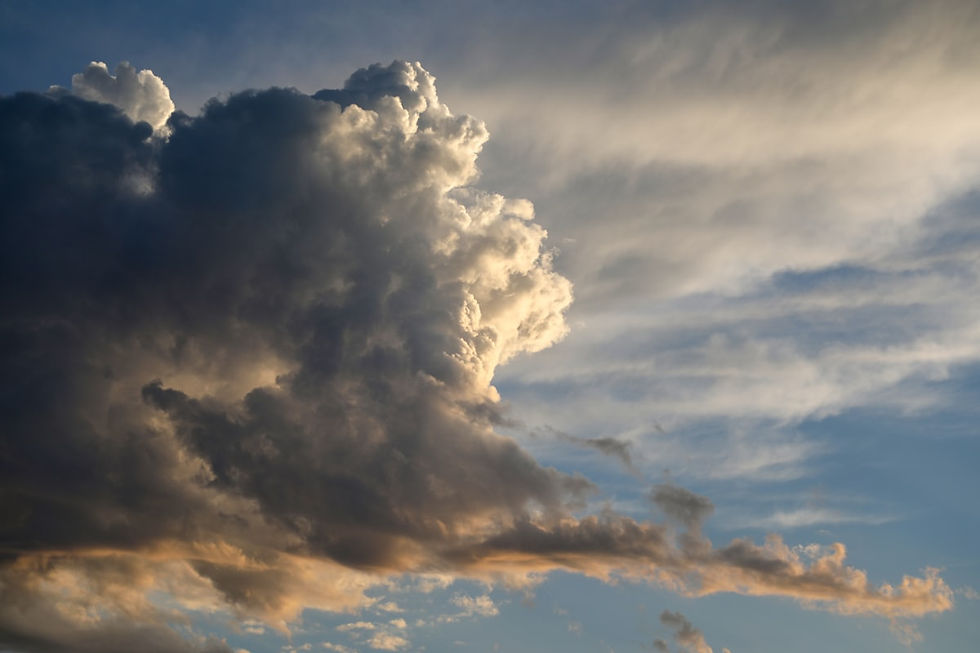 Sunlit storm clouds banking against a blue sky, dense and dark on one side, thinning into pale streaks on the other
