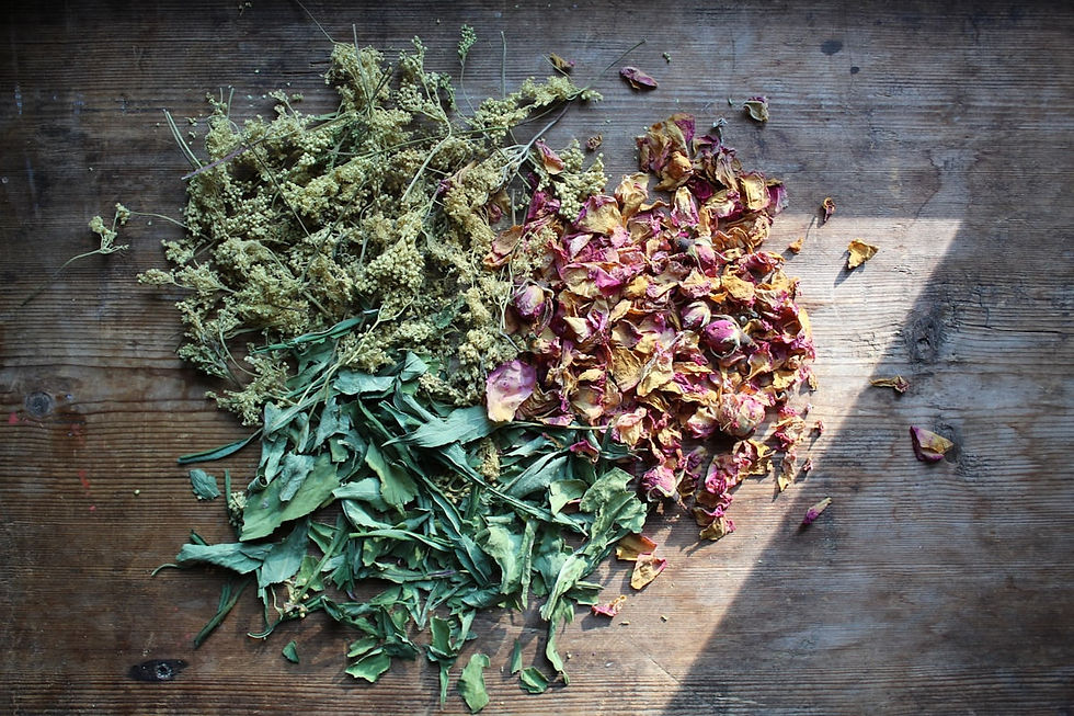 Piles of dried herbs and flower petals sorted on a wooden table, lit by a strip of sunlight