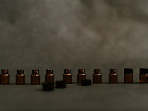 A row of small amber glass bottles against a plain grey background, most of them open with their dark caps set down in front