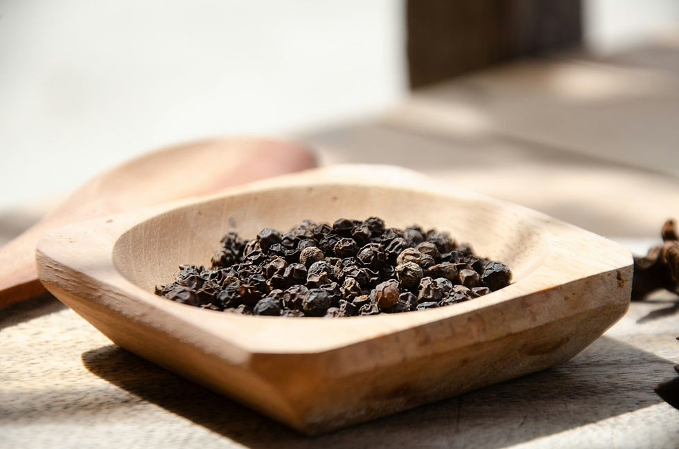 A small wooden bowl heaped with dark dried peppercorns, a wooden scoop resting just behind it
