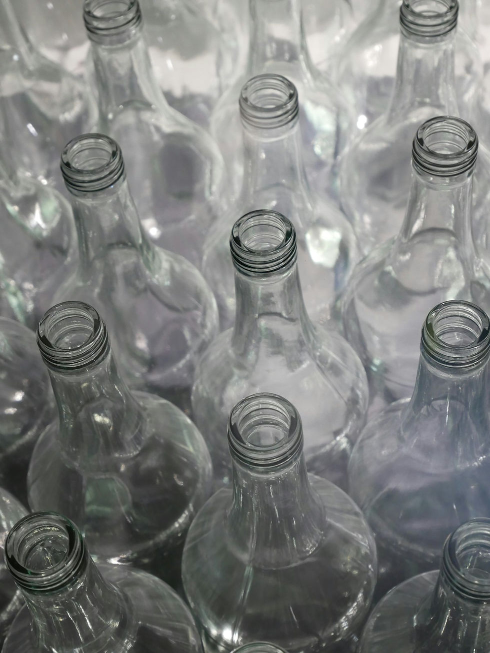 Rows of empty clear glass bottles photographed from above, catching overhead light