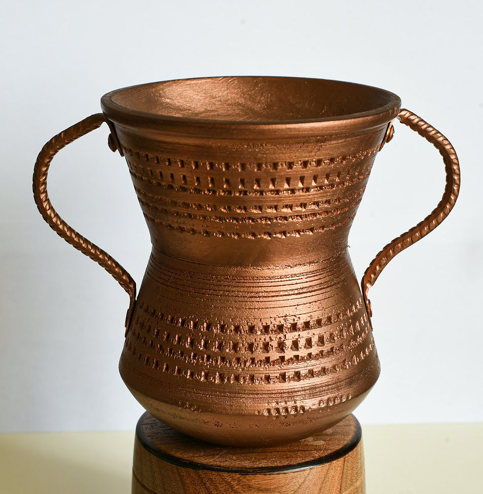 A copper vessel with a handle on each side and a stamped, dotted pattern, photographed against a plain white background on a round wooden stand