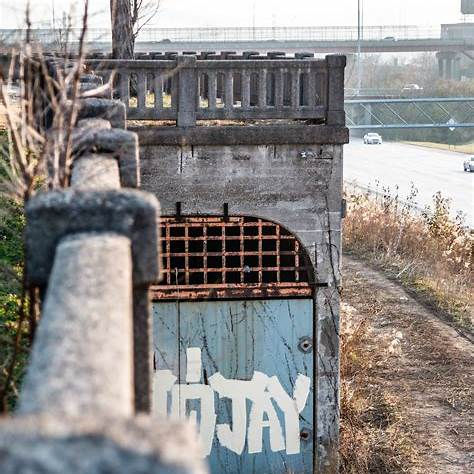 "Gated entrance to the abandoned Cincinnati subway at Brighton Place, featuring an arched concrete facade with iron bars and surrounding overgrowth."
